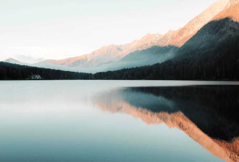 A calm alpine lake at dawn reflecting forested mountains.